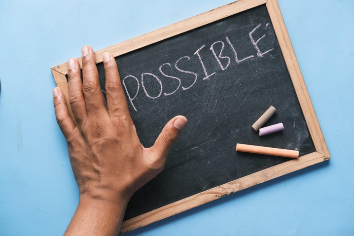 A close-up of a white board where a hand covers the “Im” of the word “impossible”
